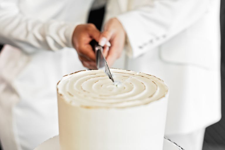 Close-up of couple cutting a simple white wedding cake with a knife.