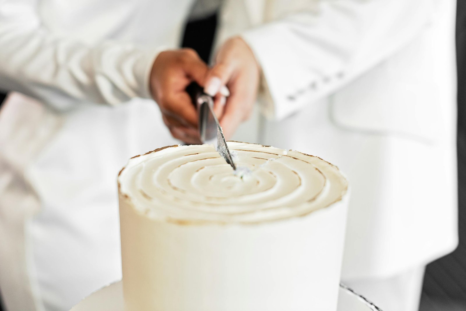 Close-up of couple cutting a simple white wedding cake with a knife.